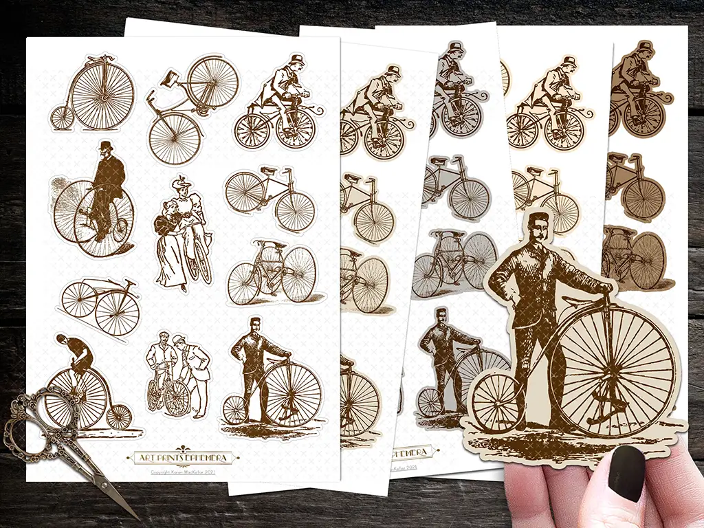 A set of sepia-toned vintage-style stickers featuring brown and white illustrations of old-fashioned bicycles and people riding them. One hand holds a cut-out sticker of a man with a penny-farthing bicycle, while scissors sit on a dark surface in the background.