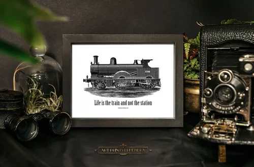 Framed black-and-white image of a vintage steam train with the text "Life is the train and not the station" on a dark table. Surrounding items include an old camera, binoculars, a potted plant, and a protective glass dome containing air plants.