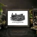 Framed black-and-white image of a vintage steam train with the text "Life is the train and not the station" on a dark table. Surrounding items include an old camera, binoculars, a potted plant, and a protective glass dome containing air plants.