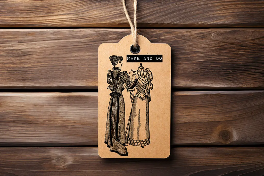 A vintage-style brown tag with a string features an illustration of two women in elaborate dresses. The label reads "MAKE AND DO" at the top. The background is a wooden surface with visible grain patterns.