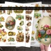 A hand holding a vintage Easter egg sticker adorned with flowers. In the background, three sheets of vintage Easter-themed stickers are visible, featuring bunnies, chicks, and floral designs. Scissors are placed on the wooden surface.